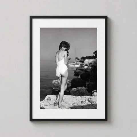 A vertical framed print of Brigitte Bardot in Saint-Tropez hanging on a light-colored wall in a minimalist living room.