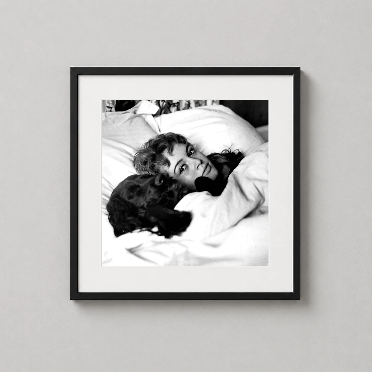 Room mockup of Brigitte Bardot in Bed with Dog Black and White Photography Print, displayed as framed wall art in a office setting as a square print with black and white tones.