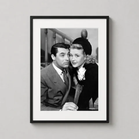 A framed Arsenic and Old Lace art print hanging in a bright home office above a wooden desk.