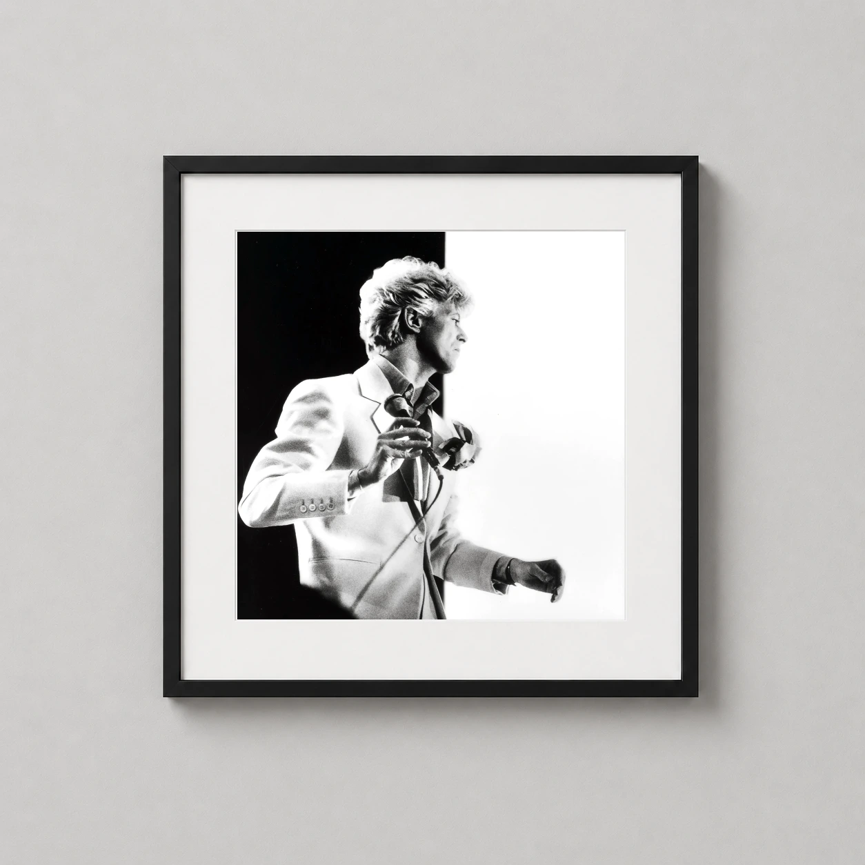 Room mockup of David Bowie Serious Moonlight Tour 1983 High Contrast Photography Print, displayed as framed wall art in a dorm room setting as a square print with black and white tones.