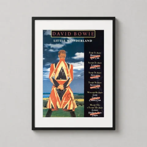 A framed David Bowie Little Wonderland tour poster hanging on a modern gallery wall above a vintage record player cabinet.