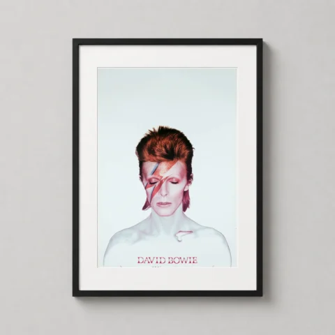 A framed Aladdin Sane art print hanging in a modern living room above a turntable and a collection of vinyl records.