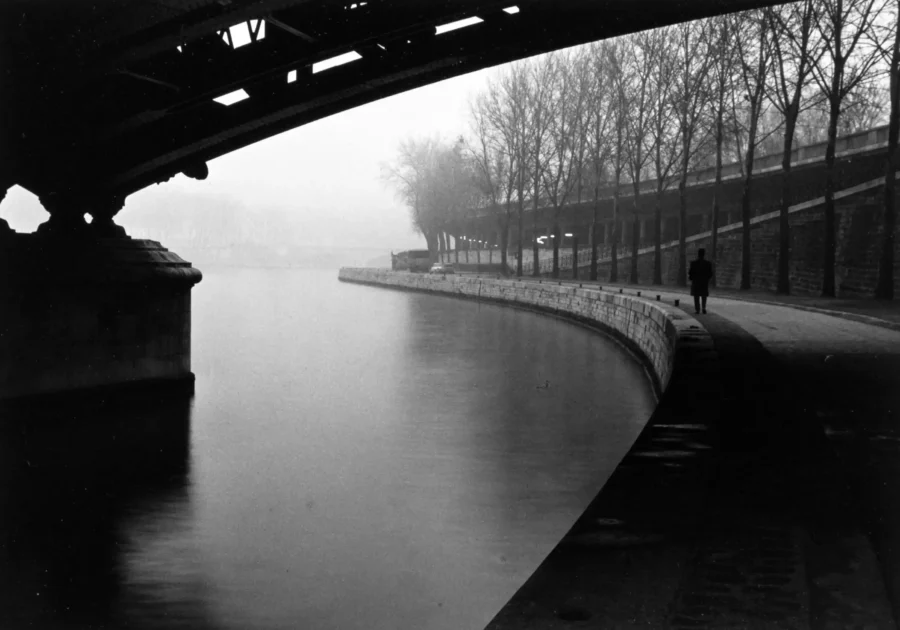 Willy Ronis poster showing a lone figure walking beside the Seine in a quiet Paris scene.